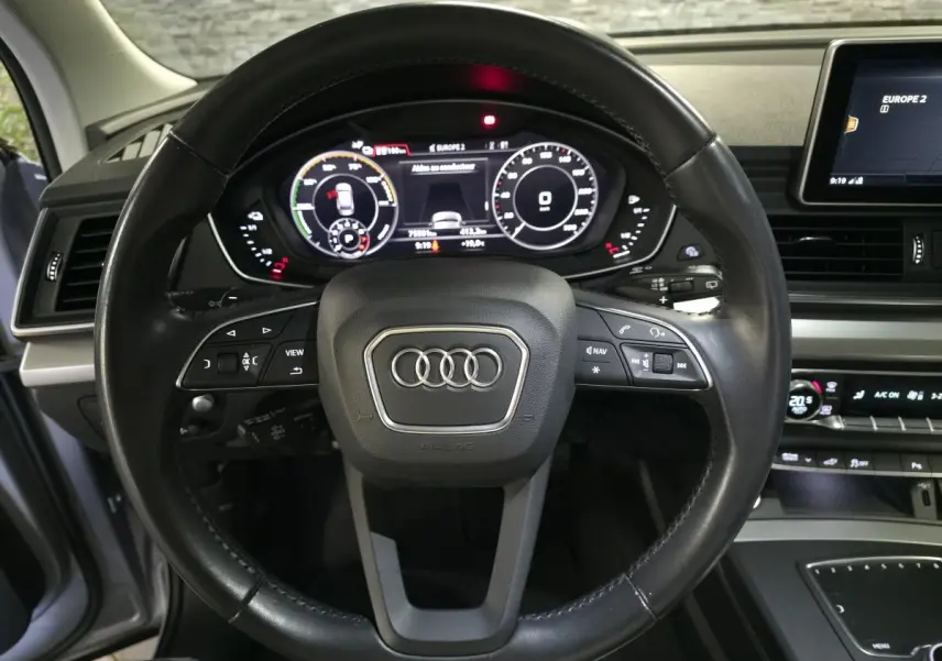 Vue centrée sur le volant cuir noir et le tableau de bord numérique de l'Audi Q5 hybride rechargeable gris de 2019.