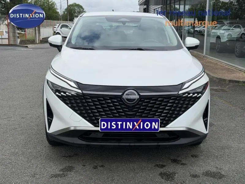 Vue de face du Nissan Qashqai blanc nacré avec calandre noire texturée et phares LED fins, sur parking extérieur.