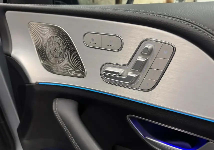 Détail de la porte côté gauche du Mercedes GLE 400 E Hybrid AMG 2023, avec commandes de siège en aluminium brossé et éclairage d’ambiance bleu.