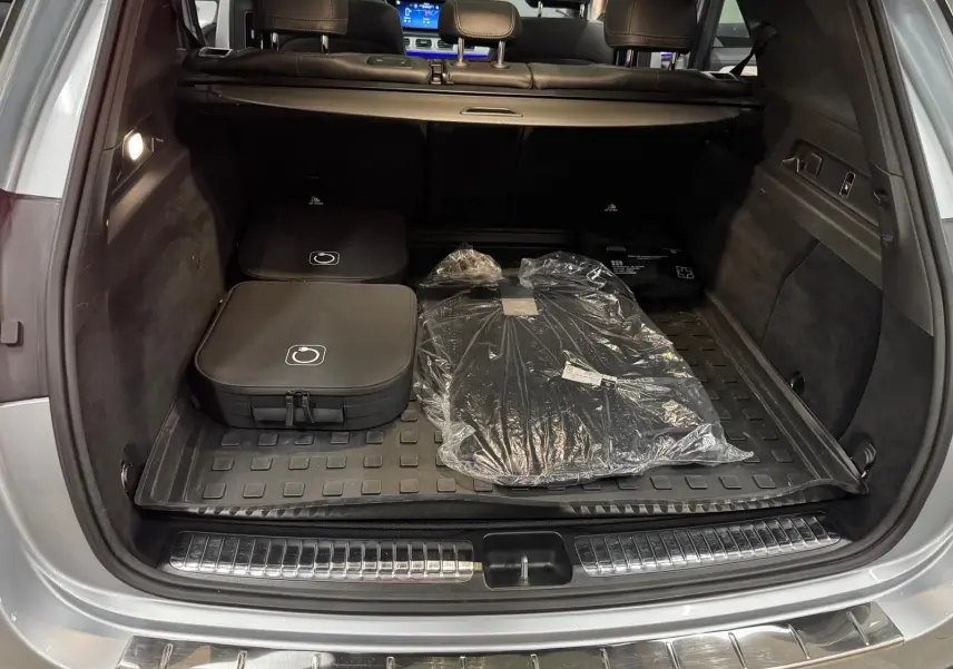 Coffre ouvert vu de l'arrière d'un Mercedes GLE 400 E Hybrid argent métallisé avec tapis et accessoires rangés.