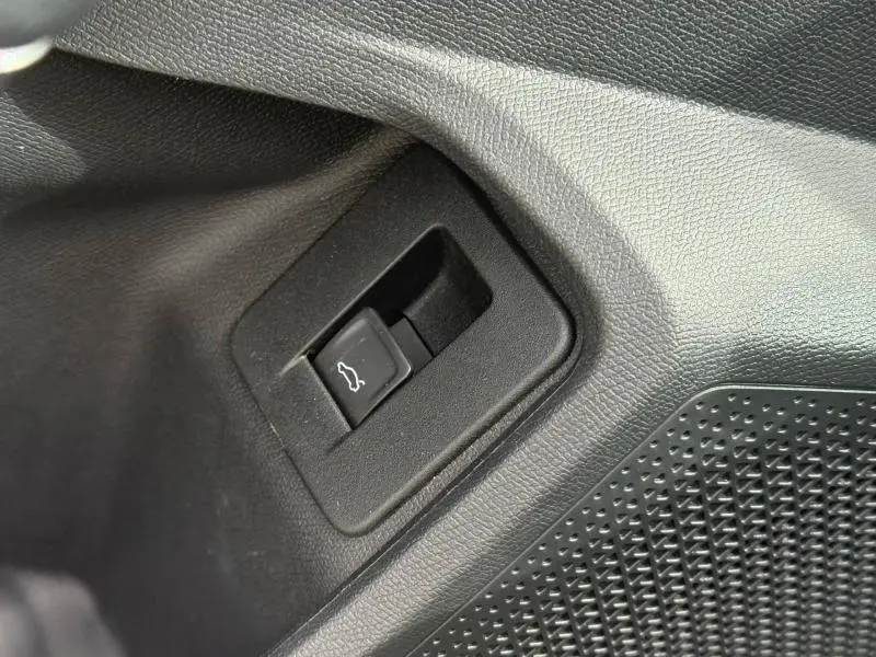 Gros plan sur le bouton d'ouverture électrique du coffre, intégré dans la garniture noire intérieure d'une CUPRA Formentor bleu.