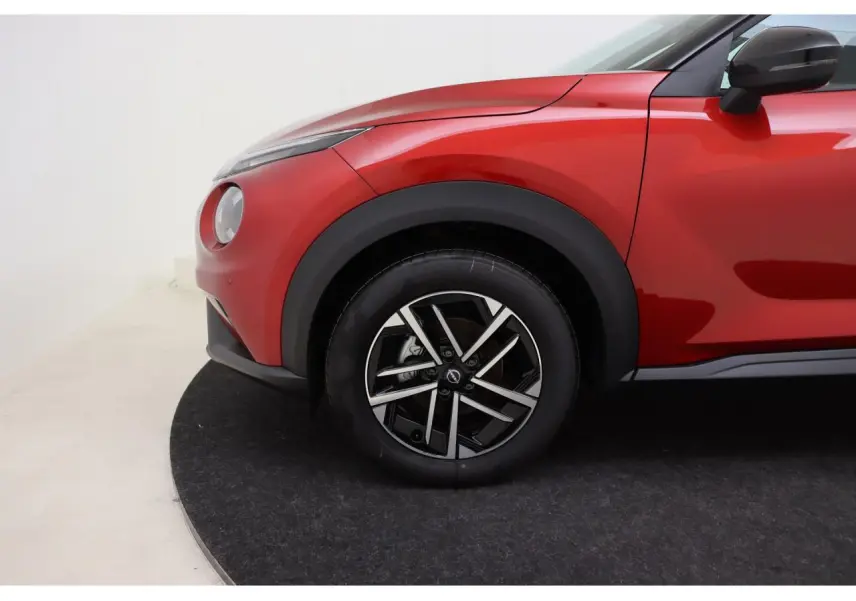Gros plan sur la roue avant gauche et l'aile d'un Nissan Juke 2026 rouge Fuji Sunset avec jante alliage 17 pouces.