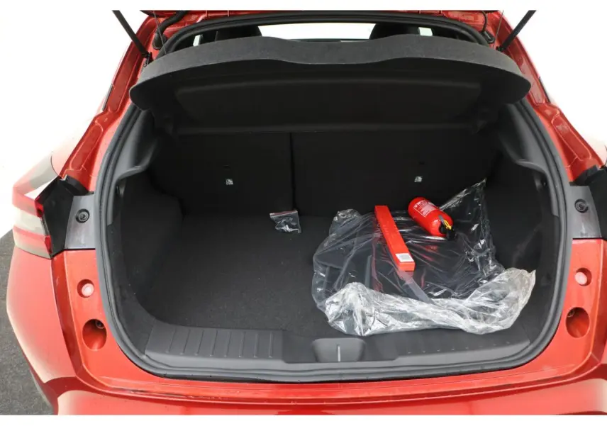 Coffre ouvert d’un Nissan Juke rouge Fuji Sunset, montrant un espace de rangement avec extincteur et triangle de signalisation.