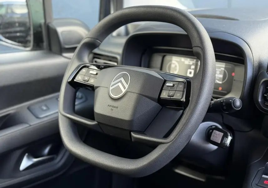 Vue rapprochée du volant multifonctions noir du Citroën Berlingo 2025, avec tableau de bord numérique en arrière-plan.