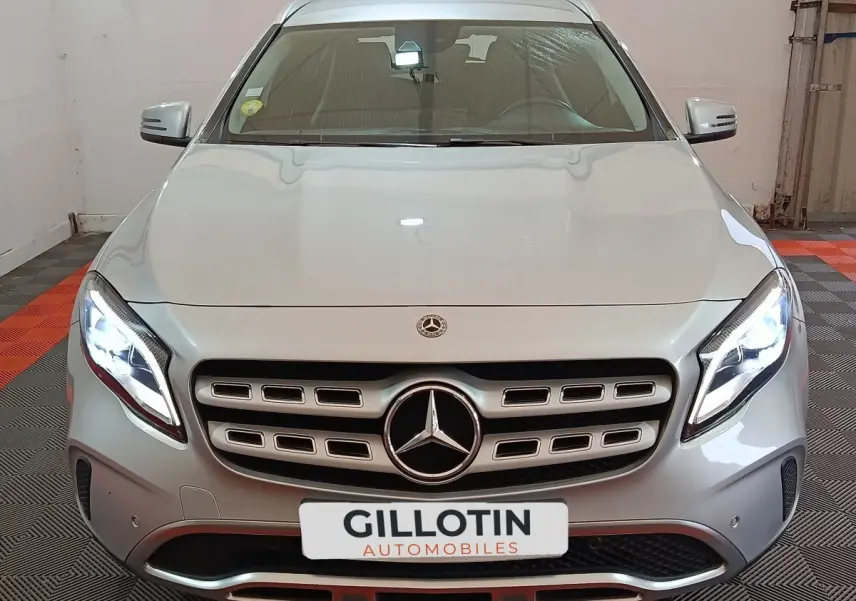 Vue frontale d'un Mercedes GLA 200 d gris clair avec phares LED allumés et calandre distinctive en showroom.