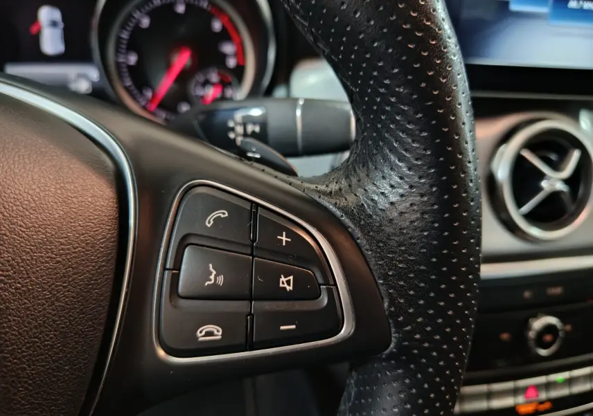 Gros plan sur les commandes gauche du volant cuir perforé du Mercedes GLA 200 d gris clair, avec tableau de bord en arrière-plan.