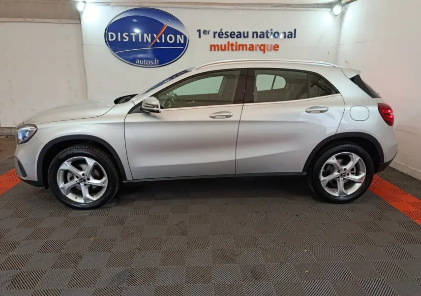 Profil côté gauche d'un Mercedes GLA 200 d Business Executive gris clair, en intérieur sur sol damier avec logo Distinxion en arrière-plan.