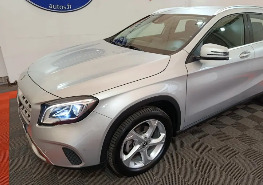 Vue 3/4 avant droit d'une Mercedes GLA 200 d Business Executive gris clair avec phares LED allumés et jantes alliage.