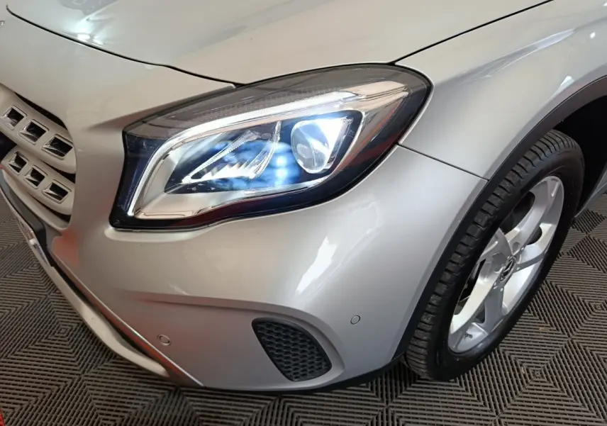 Gros plan sur l'avant droit gris clair d'une Mercedes GLA 200 d avec phares LED allumés et jante alliage visible.