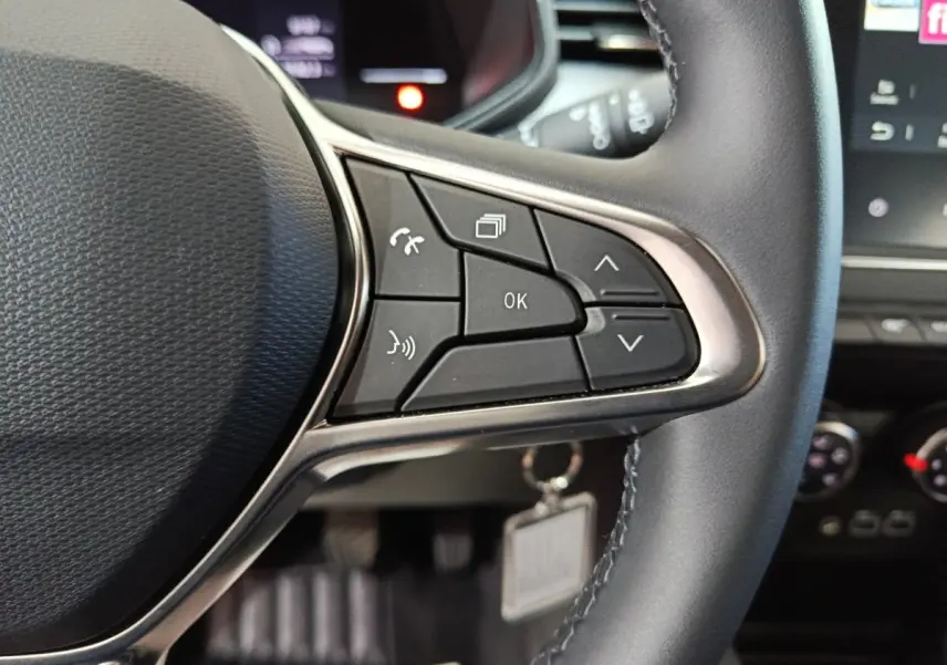 Gros plan sur le volant cuir noir de la Renault Clio gris clair, avec commandes multifonctions au volant visibles.