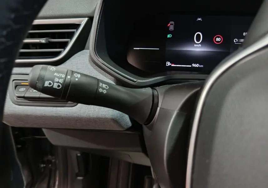 Vue rapprochée du combiné d'instruments numérique et du commodo des phares dans le tableau de bord gris clair de la Renault Clio 2025.