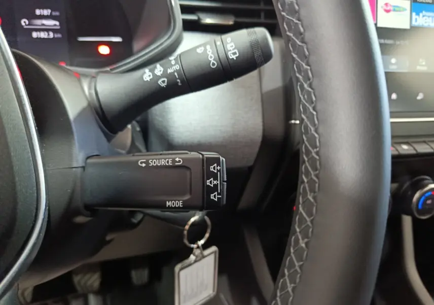 Gros plan sur le volant cuir et les commandes au volant de la Renault Clio gris clair, affichage multifonctions visible en arrière-plan.