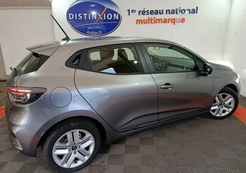 Vue latérale droite d'une Renault Clio gris clair 2025 garée en intérieur, avec jantes alliage et feux arrière LED allumés.