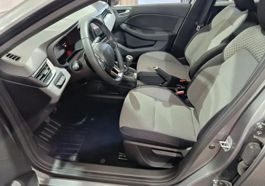 Vue intérieure côté conducteur de la Renault Clio gris clair 2025, montrant sièges tissu et tableau de bord moderne.