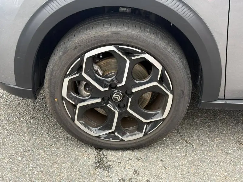 Gros plan sur la roue avant droite d'une Citroën C3 électrique 2025 en Gris Mercury avec jante noire et argentée au design géométrique.