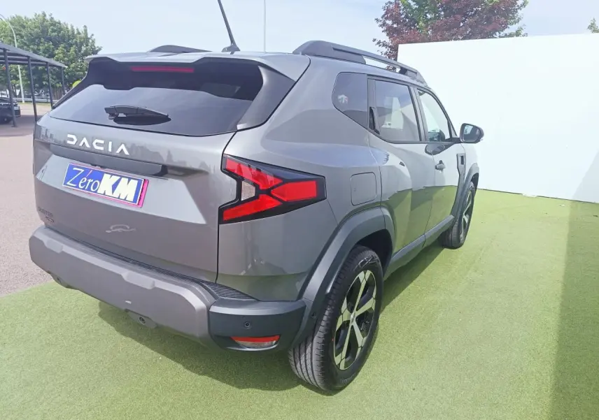 Vue 3/4 arrière droite du Dacia Duster gris schiste métallisé avec jantes alliage diamantées et barres de toit noires.