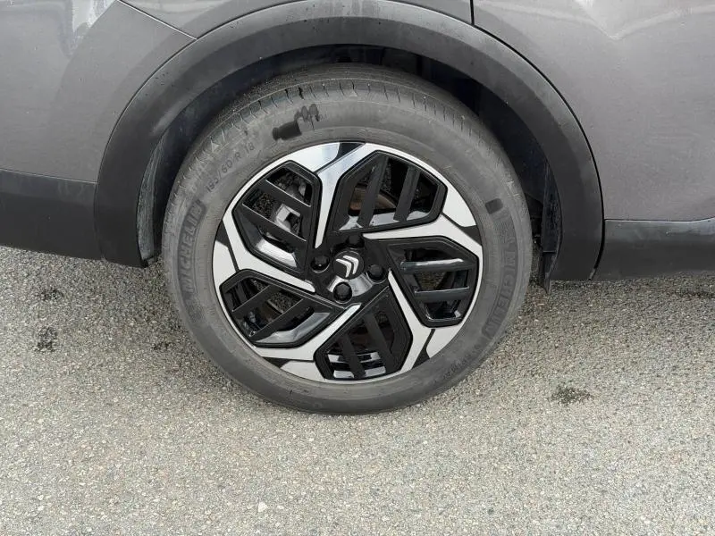 Gros plan sur la roue avant droite du Citroën C4 X 2024 gris Platinium avec jante alliage noire et argentée au design géométrique.