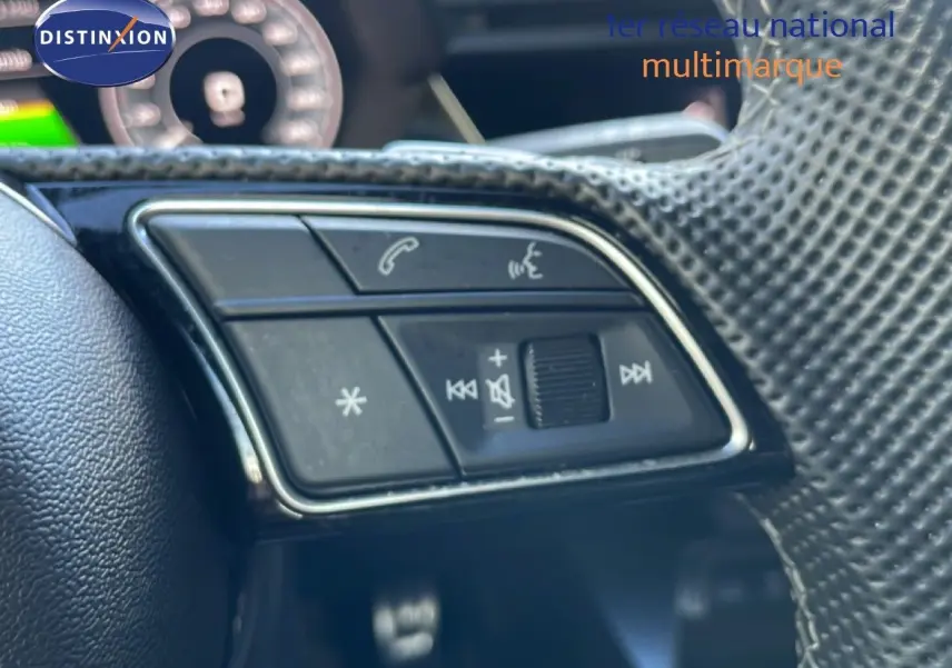 Gros plan sur les commandes multifonctions côté gauche du volant d’un Audi A3 Sportback blanc Ibis 2025.
