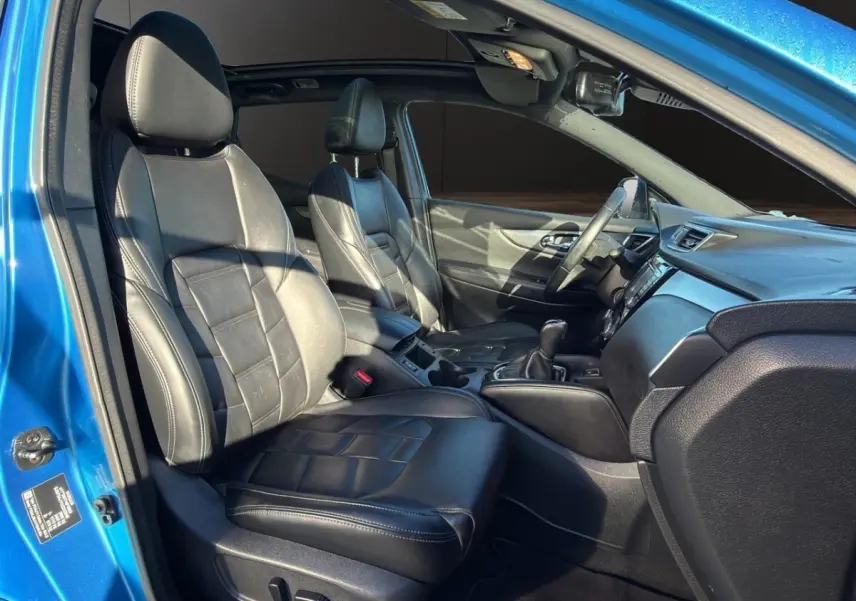 Vue intérieure côté gauche du Nissan Qashqai bleu 2018, mettant en valeur les sièges avant en cuir noir et le tableau de bord.