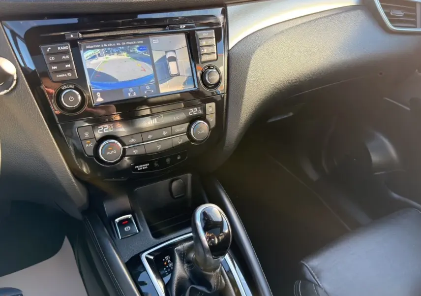 Vue intérieure centrée sur la console centrale du Nissan Qashqai bleu, avec écran tactile et levier de boîte automatique.