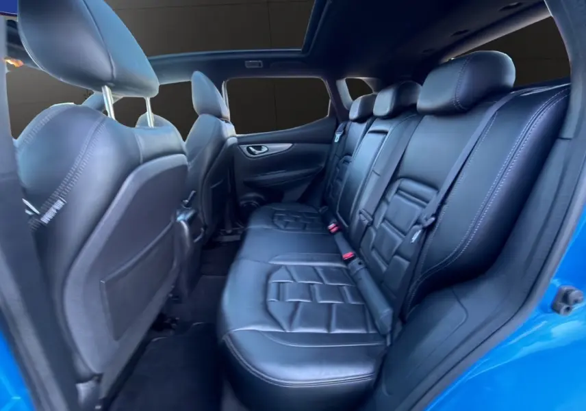 Vue intérieure arrière du Nissan Qashqai bleu 2018, sièges en cuir noir et toit ouvrant panoramique visible.