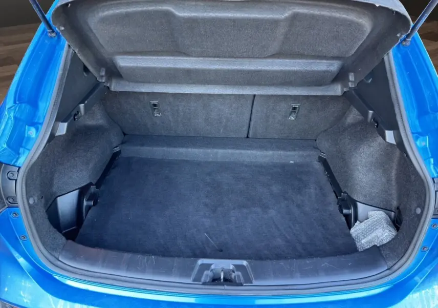 Vue plongeante sur le coffre ouvert d’un Nissan Qashqai bleu, montrant un espace de rangement propre et spacieux.