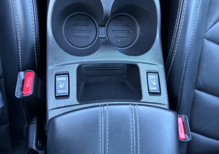 Gros plan sur la console centrale noire du Nissan Qashqai Tekna+ avec commandes chauffantes sièges et porte-gobelets.