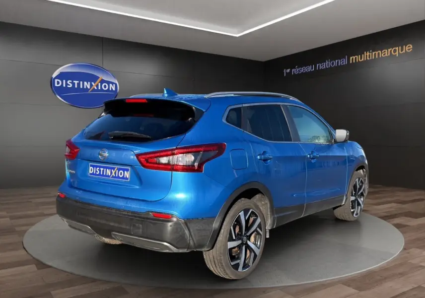 Vue 3/4 arrière droite d'un Nissan Qashqai bleu métallisé avec jantes alliage et toit avec rails chromés.