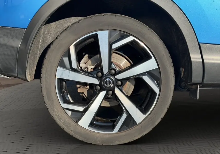 Gros plan sur la roue avant droite du Nissan Qashqai bleu, jante alliage à design moderne bicolore.