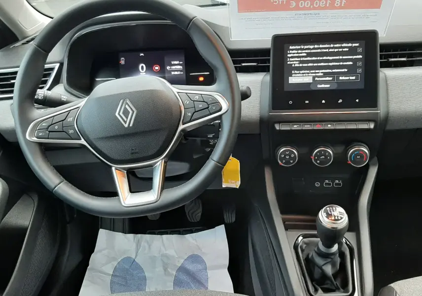 Intérieur de Renault Clio V TCE 90ch Evolution 2025, vue du poste de conduite avec volant, écran tactile et levier de vitesse manuel.