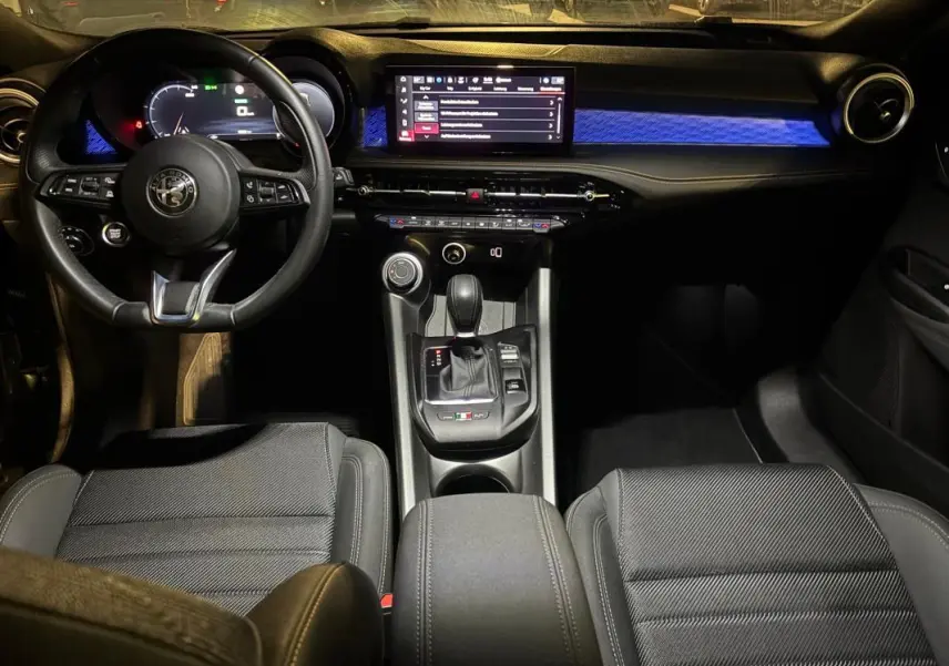 Vue intérieure avant de l'Alfa Romeo Tonale 2023 avec tableau de bord noir et éclairage bleu sur la planche de bord.