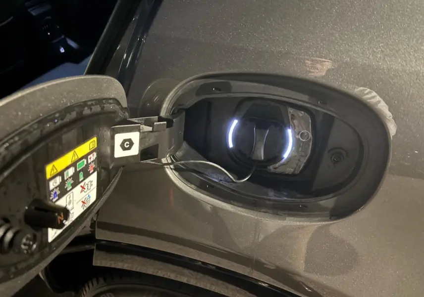 Gros plan sur la trappe de recharge ouverte côté gauche d'une Alfa Romeo Tonale grise 2023 avec câble de charge connecté.