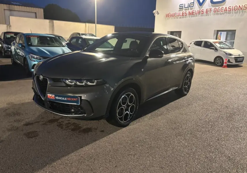 Vue 3/4 avant droit d'une Alfa Romeo Tonale gris métallisé avec jantes alliage 18 pouces, stationnée de nuit.