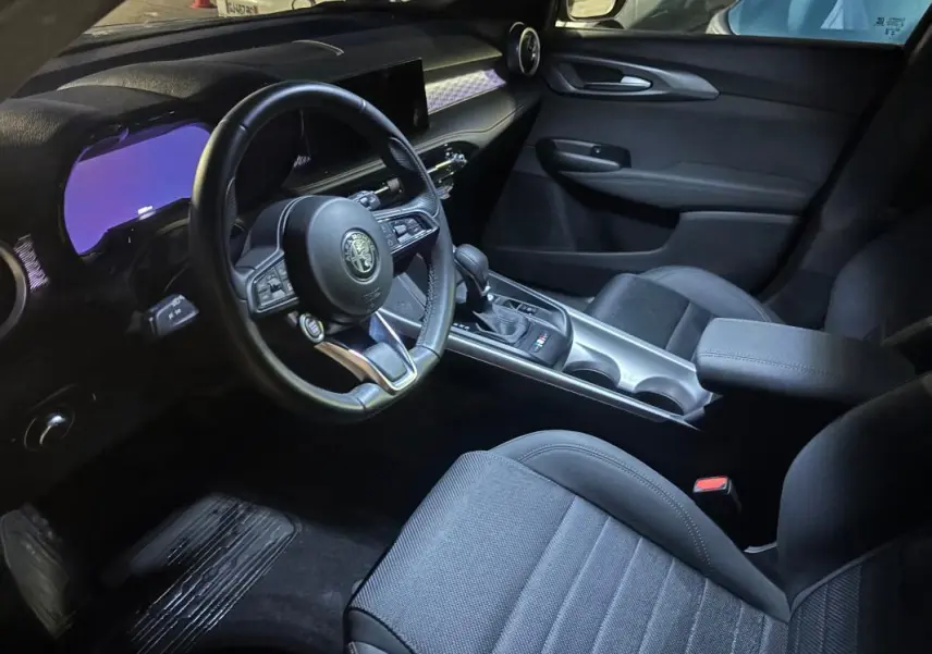 Vue intérieure côté conducteur de l'Alfa Romeo Tonale 2023, montrant le volant sport, la console centrale et les sièges noirs.