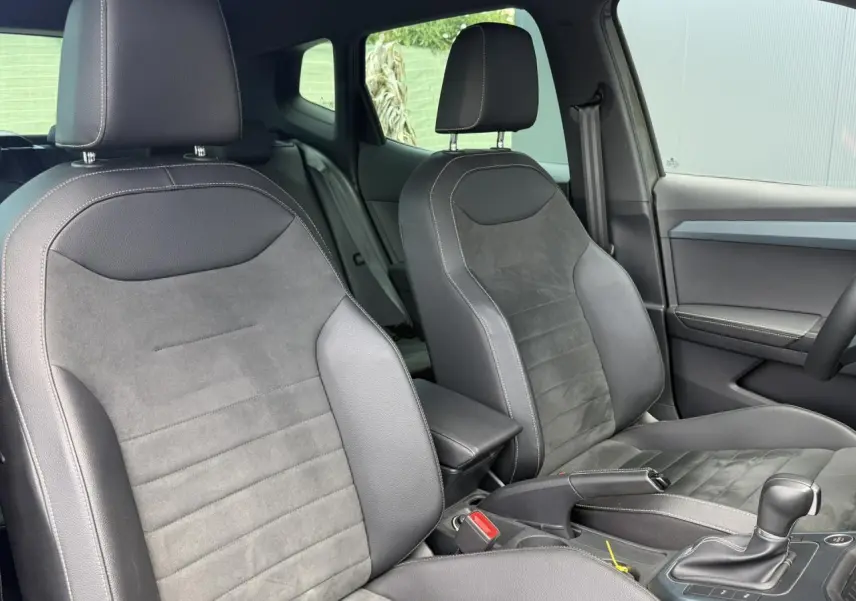 Vue intérieure des sièges avant en cuir-alcantara noir du SEAT Arona TSI 115 DSG Xpérience 2025, avec console centrale et levier de vitesse.