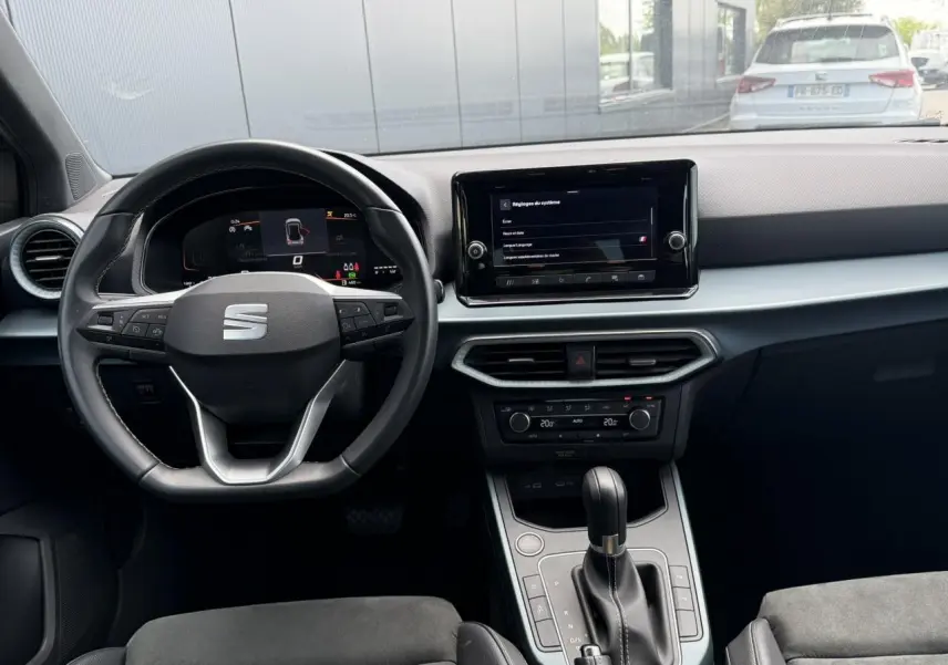 Vue intérieure frontale du poste de conduite du SEAT Arona gris, avec volant multifonction et écran tactile central.