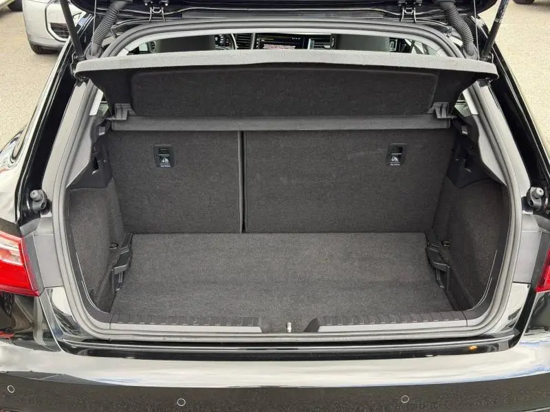 Coffre ouvert vu de l'arrière d'une Audi A1 Sportback 25 TFSI noir Mythic métallisé, intérieur du coffre en tissu gris.