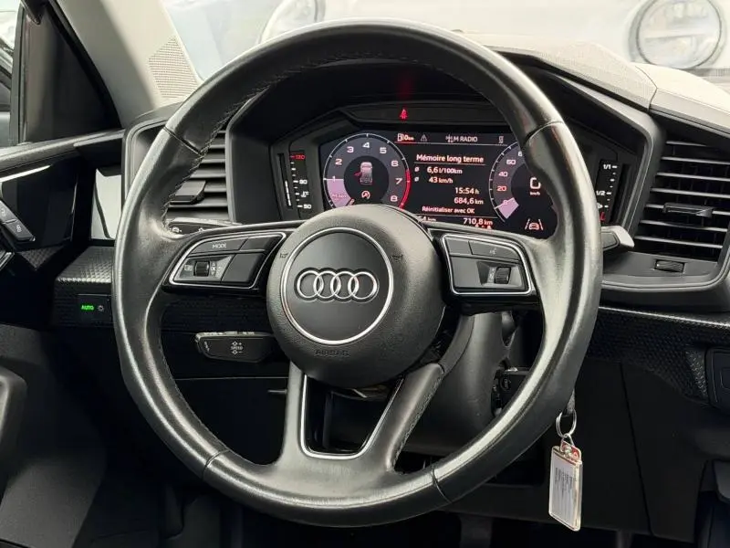 Vue rapprochée du volant Audi A1 Sportback 2023 en cuir noir avec tableau de bord numérique affichant les informations de conduite.