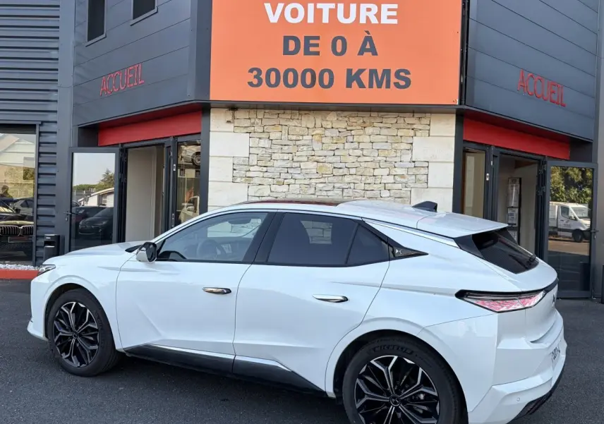 Vue côté gauche arrière d'une DS4 blanche 2024 avec jantes noires, stationnée devant un bâtiment commercial.
