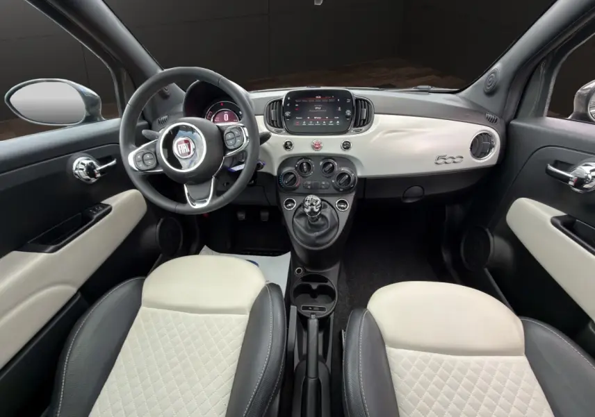 Vue intérieure avant de la Fiat 500 avec tableau de bord blanc, volant cuir multifonctions et sièges bicolores noirs et blancs.