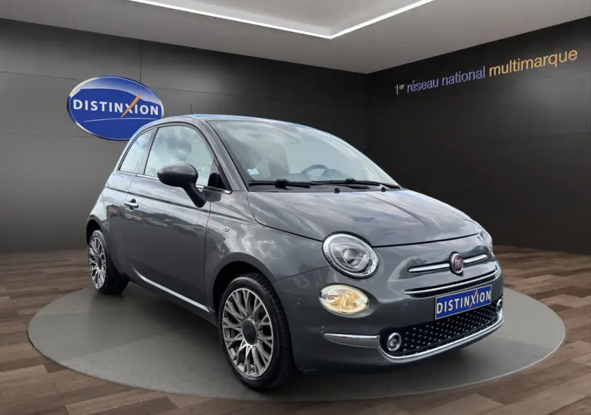 Fiat 500 gris foncé vue 3/4 avant avec phares ronds et jantes alliage détaillées sur fond showroom.