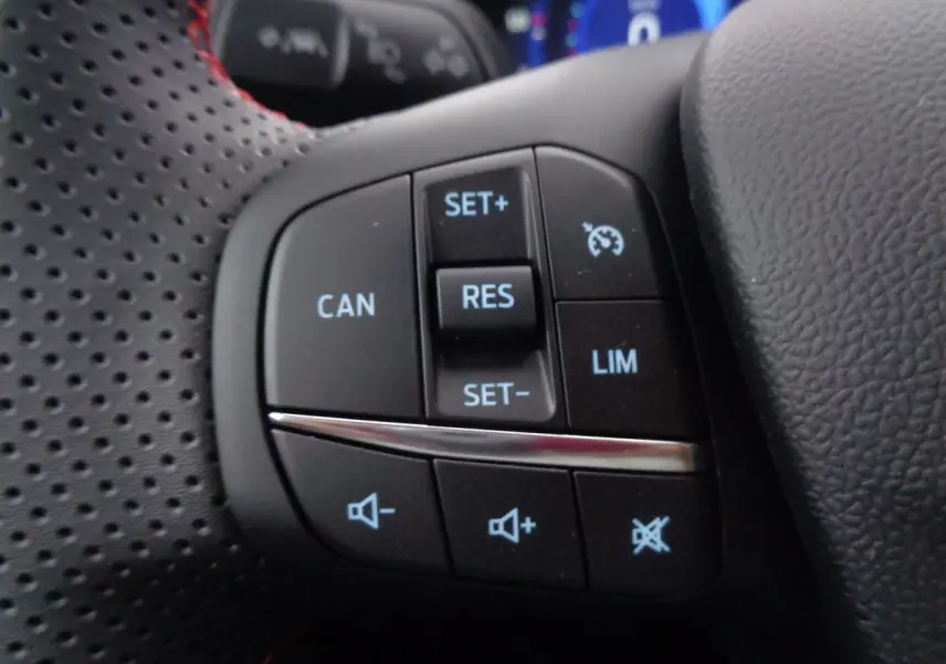 Gros plan sur les commandes du volant perforé noir du Ford Puma blanc, montrant les boutons de régulateur et volume.