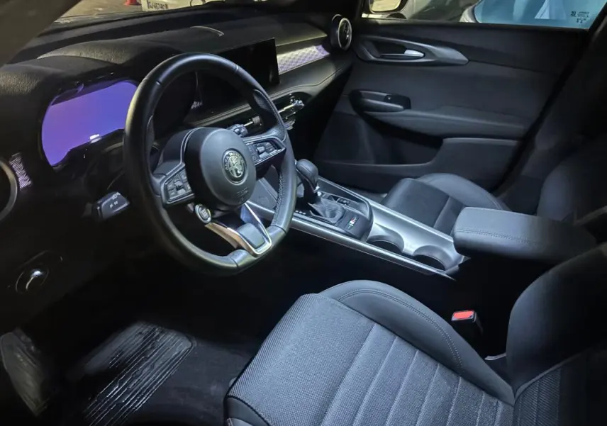 Intérieur de l'Alfa Romeo Tonale 2023 vu côté conducteur, volant sport, console centrale avec boîte auto et accoudoir.