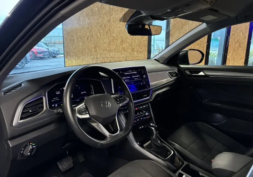 Vue intérieure côté conducteur du Volkswagen T-Roc 2023 avec tableau de bord noir et écran tactile central allumé.