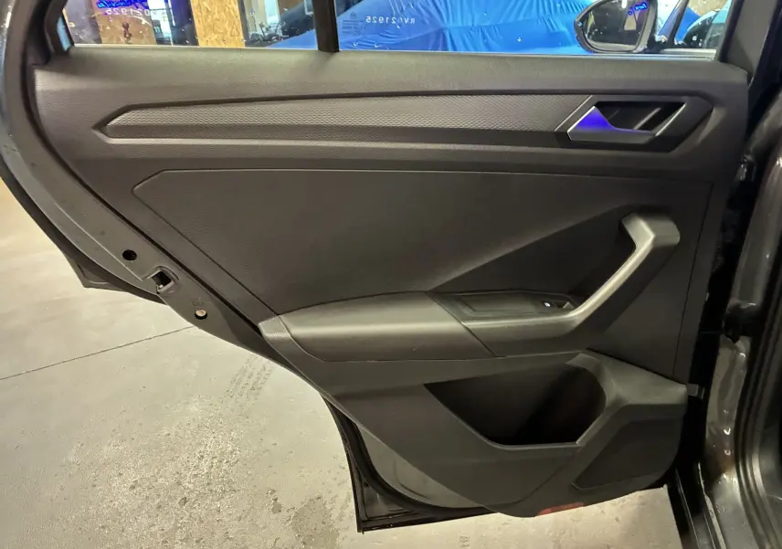 Vue intérieure de la porte arrière gauche du Volkswagen T-Roc gris 2023, avec poignée et commandes de fenêtre visibles.