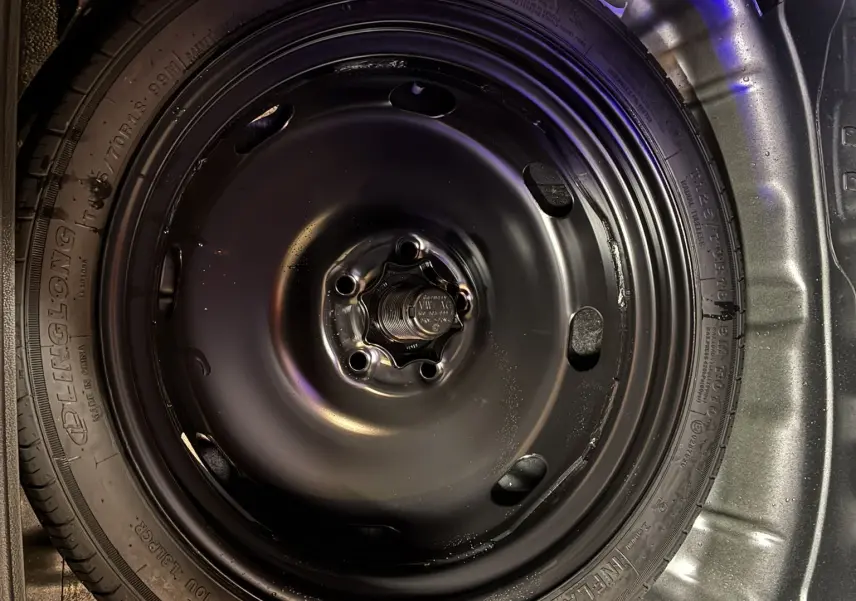 Gros plan sur la roue de secours noire dans le coffre d’un Volkswagen T-Roc gris 2023, version essence.