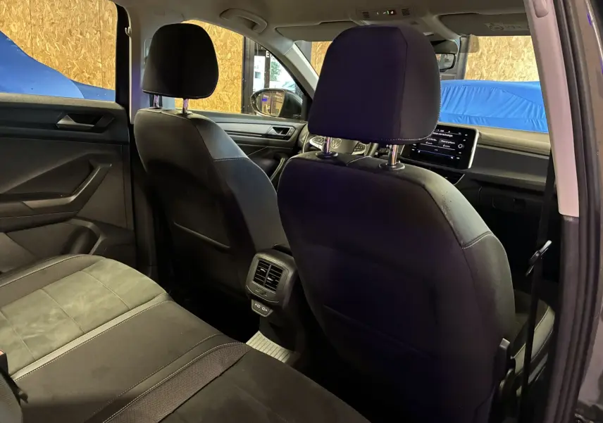 Vue intérieure arrière du Volkswagen T-Roc gris 2023, mettant en valeur les sièges en tissu noir et l'écran tactile du tableau de bord.
