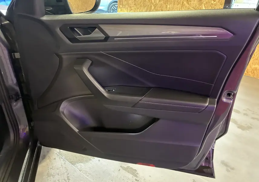 Vue intérieure de la porte côté gauche du Volkswagen T-Roc gris 2023, avec garniture noire et surpiqûres blanches.