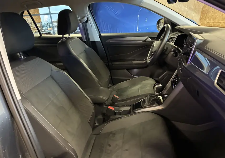 Vue intérieure côté gauche du Volkswagen T-Roc gris 2023, montrant les sièges noirs en tissu et la console centrale avec écran tactile.