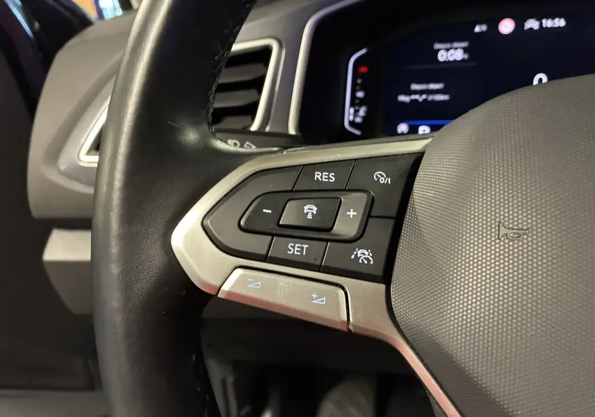 Gros plan sur le volant noir du Volkswagen T-Roc 2023, montrant les commandes de régulateur de vitesse à gauche.